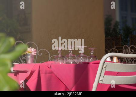 Clean upturned wine glasses on a pink tablecloth. Table setting. Empty restaurant terrace, siesta. Stock Photo