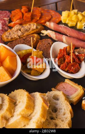 Sliced sausage and cheese on a brown background. Italian antipasti wine snacks set. Cheese, Mediterranean olives, Prosciutto  with melon, bread sticks Stock Photo