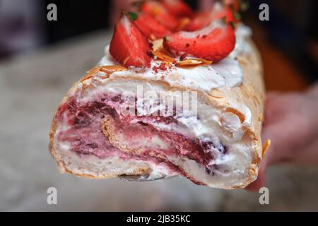 Meringue roll decorated with creamy cream and slices of fresh strawberries in a cut. Stock Photo