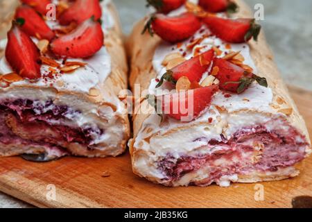 Meringue roll decorated with creamy cream and slices of fresh strawberries in a cut. Stock Photo