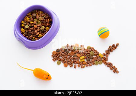 shape of fish made with dry pet food near purple bowl and toys isolated on white Stock Photo