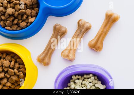 close up view of bone shaped pet treats near bowls with dry pet food and cookies isolated on white Stock Photo