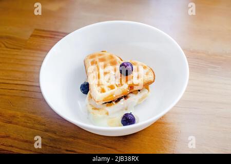 Tasty homemade Belgian waffles heart shaped on white bowl with berries and condensed milk. Dessert for valentine's day. Stock Photo