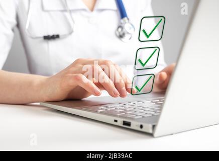 Doctor working on laptop and taking survey, ticking answers at screen. Woman in lab coat sitting at table with computer. Health care, medicine concept. High quality photo Stock Photo