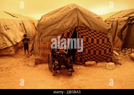 Idlib City, Syria. 02nd June, 2022. A man sits in a wheelchair near the tents of a camp for displaced people during a sandstorm hitting the Idlib Province. Credit: Anas Alkharboutli/dpa/Alamy Live News Stock Photo