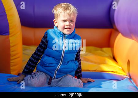 A portrait of a little boy wearing a blue vest on a colorful striped trampoline. The child squats for a little rest. Stock Photo