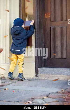 Little boy, checking the mail in outdoors mailbox. The kid is waiting for the letter, checks the correspondence and looks into the metal mailbox. Fall Stock Photo