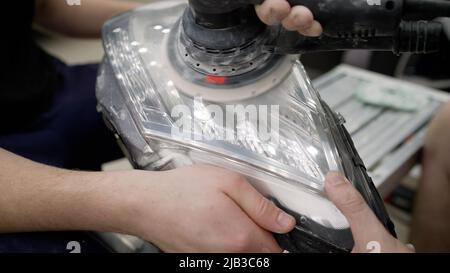 The process of polishing the headlights of an expensive car. The master polishes the headlight of the car with the help of a typewriter. Master mechan Stock Photo