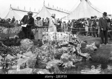 1929, historical, people dressed in the formal clothes and hats of the era attending the Chelsea Flower Show, London, England, UK, with judges studying a rocky pool feature. Stock Photo