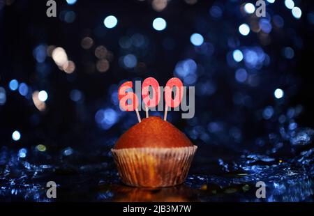 Digital gift card birthday concept. Tasty homemade vanilla anniversary cupcake with number 600 six hundred on aluminium reflecting foil and blurred background in minimalistic style. High quality image Stock Photo