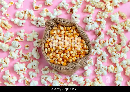 Corn grains in a bag. Scattered popcorn on a pink background. Top view. Stock Photo
