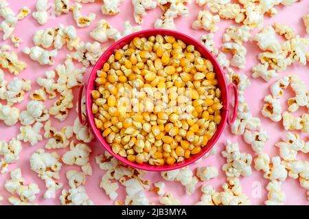 Corn grains in a bowl. Scattered popcorn on a pink background. Top view. Stock Photo