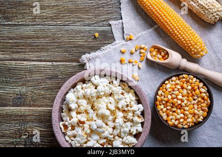 Corn kernels, cob, freshly popped popcorn on wooden background with copy space. Cooking popcorn. Stock Photo