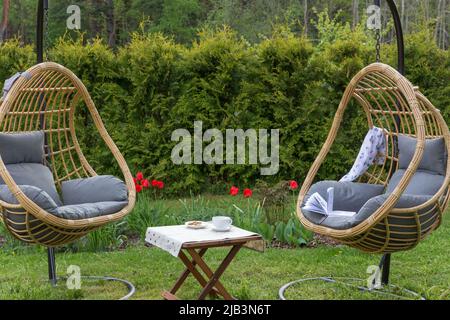 Rattan garden swing with cushion in the garden, seating area in the yard. Summer vacation concept. Stock Photo