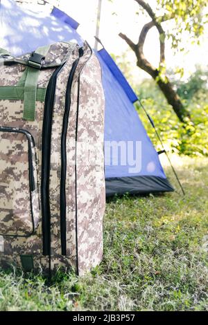 Defocus blue open tourist tent standing on green nature background. Army backpack. Tourism concept. Summer vacation in forest, camping. Wild nature. H Stock Photo