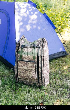 Defocus blue open tourist tent standing on green nature background. Army backpack. Tourism concept. Summer vacation in forest, camping. Lifestyle. Hik Stock Photo