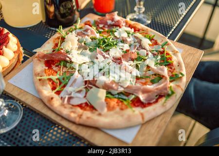 Served banquet table with fresh traditional italian pizza with ham, cheese, tomatoes and arugula on a wooden boards in a street cafe Stock Photo