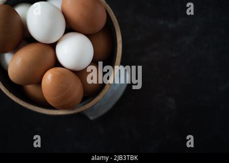 Top view of ceramic bowl of fresh organic brown and white eggs on dark background. Stock Photo