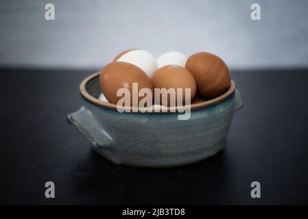 Side view of handmade ceramic bowl of fresh organic brown and white eggs on dark and concrete background. Stock Photo