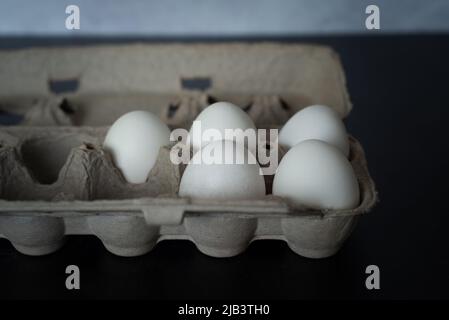 Half carton of fresh white eggs on dark background with concrete wall. Stock Photo