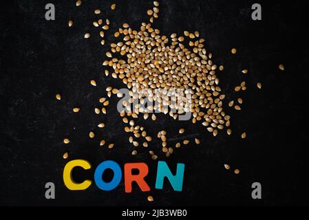 Top view of corn kernels with wooden colored letters spelling CORN on dark moody background. Stock Photo