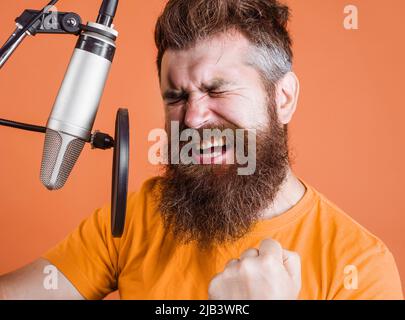 Bearded man sings in condenser microphone at recording studio. Emotional Male professional vocalist. Stock Photo