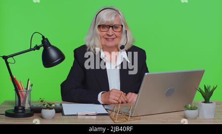 Senior businesswoman wear wireless headset make conference video call on laptop. Female elderly professional call center agentoperator having distance webcam chat job interview on computer in office Stock Photo