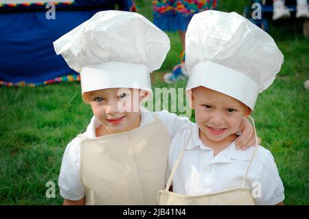 Twin kids children looking alike and like cooks with tall hats Stock Photo