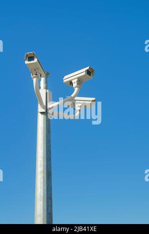 Three CCTV security cameras mounted atop a pole against a clear blue sky Stock Photo