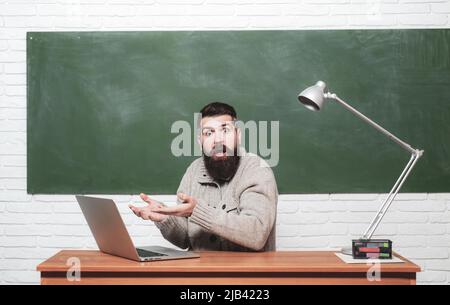 Science and education concept. Knowledge day. Student working on laptop in college. Young teacher near chalkboard in school classroom. Chalkboard for Stock Photo