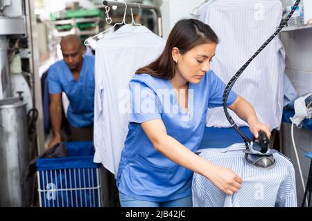 Woman laundry worker ironing shirt at dry-cleaning Stock Photo