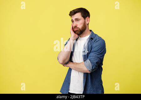 Upset man thoughtfully holding his beard on yellow background Stock Photo