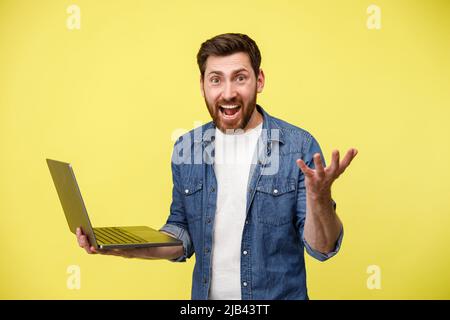 Emotional man holding a laptop and shouting actively gesturing with his hands Stock Photo