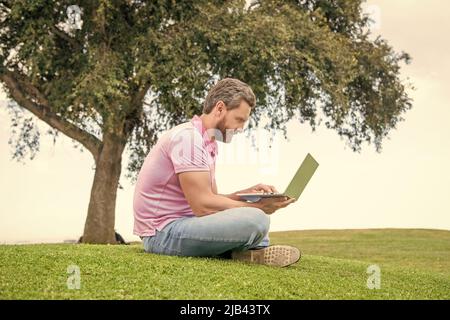 freelance man post blog online sit on grass. writing online. businessman using laptop for blogging. Stock Photo