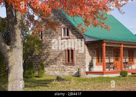 Old circa 1850 Canadiana cottage style cut stone home with green sheet metal roof in autumn. Stock Photo