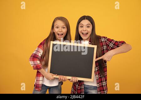 amazed kids in casual checkered point finger on school blackboard for copy space, advertisement Stock Photo