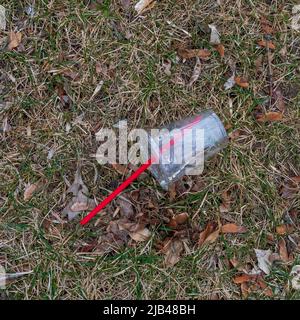 An empty, discarded plastic drinking cup lays on springtime grass near a curb. Stock Photo