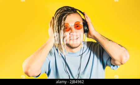 Young handsome man in sunglasses, headphones listening to music, singing. Positive cheerful guy with blonde dreadlocks dancing, enjoying songs through Stock Photo