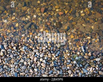 Pebbles at a natural river shore from above. Top down view on small stones with dirt and water. Background texture with a smooth transition. Stock Photo