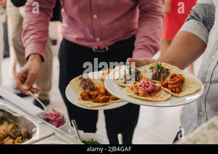 Two men eating tacos at a buffet, they are preparing their food and  serving, at a Mexican wedding or party Stock Photo - Alamy