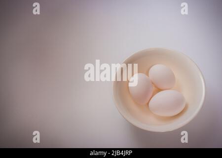 Three eggs on bowl on plain white background with copy space. Stock Photo