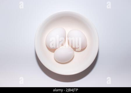 Three eggs on bowl from vertical view on plain white background. Stock Photo