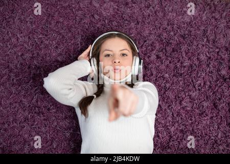 A girl listens to music and sings while lying on the carpet at home. Stock Photo