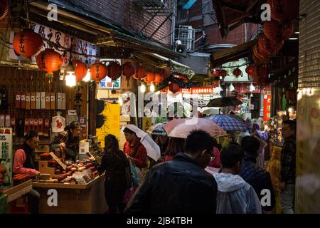 Jiufen, Taiwan - Dec 19 2019 : The shopping street of Jiufen in rainy day. There are many tourist walking with umbrella in image. Stock Photo