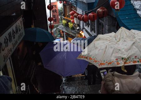 Jioufen, Taiwan - Dec 19 2019 : The image of shopping street of Jioufen in rainy day. There are many tourist walking with umbrella in image. Stock Photo