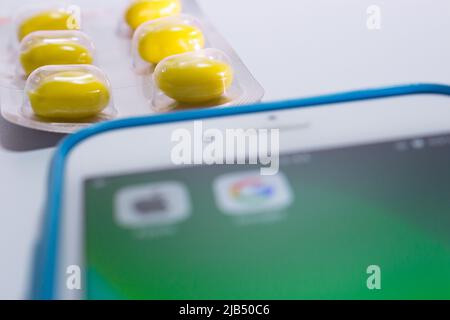 Kumamoto, Japan - May 7 2020 : Concept image of blured Apple & Google logo on iPhone screen with pills on white background. Stock Photo
