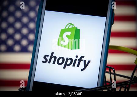 Logo of Shopify, a Canadian multinational e-commerce (online stores & retail point-of-sale systems) company, on iPhone in shopping cart with US flag Stock Photo
