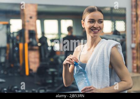 Indoor gym portrait of a young cheerful caucasian adult woman smiling and closing the water bottle. Wellbeing concept. High quality photo Stock Photo