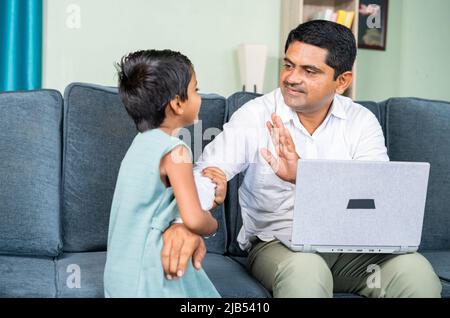 little daughter disturbing by pullinf her father while busy working on laptop at home during coronavirus covid-19 pandemic - concept of work from home Stock Photo