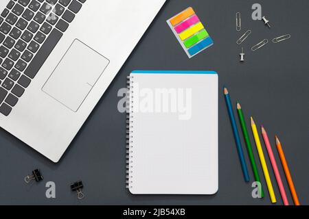 Workplace in the office. Gray table. The photo shows a laptop, colorful stickers, pencils, office accessories. Multicolored pencils lie near the noteb Stock Photo